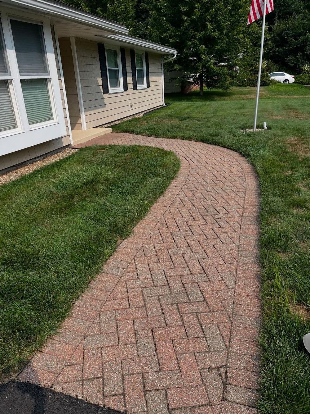 Curved brick walkway leading to a house with lush green lawn and American flag.