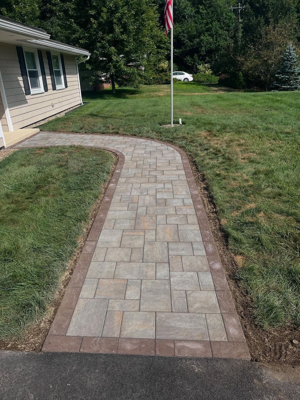 Curved stone pathway leading to a house with grass and an American flag nearby.